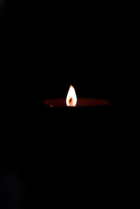 A candle flame glowing softly against a dark background, symbolizing memory and hope.