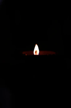 A softly glowing golden candle flame against a deep black background with subtle shimmering accents.