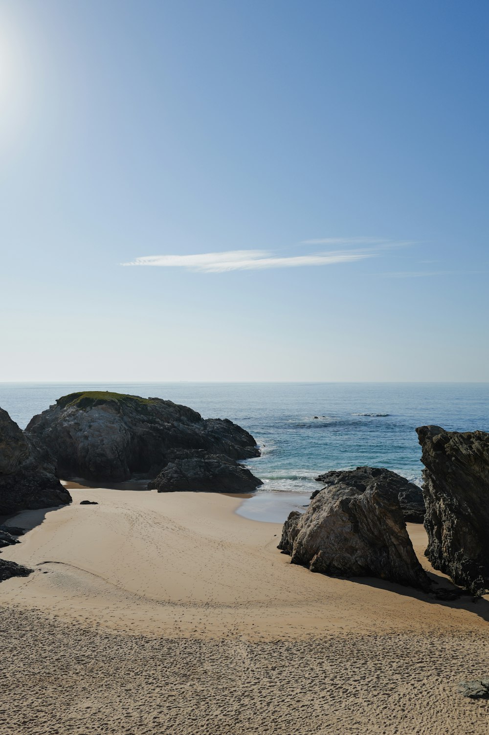 a sandy beach next to the ocean under a blue sky