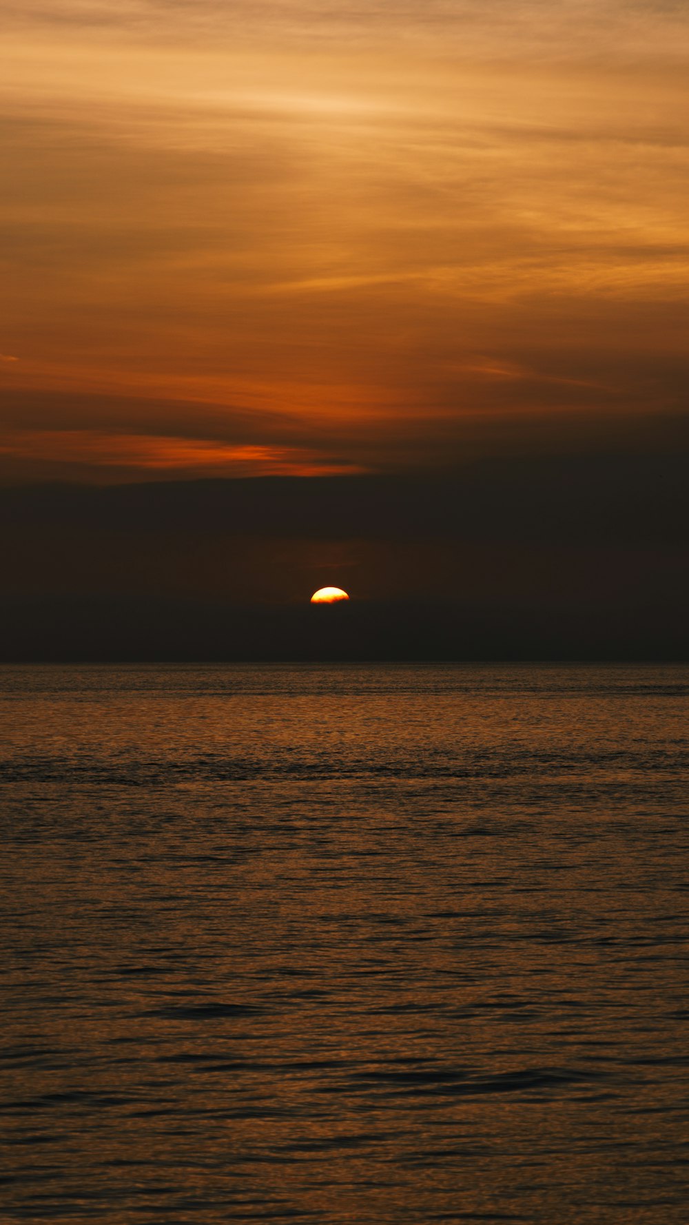 the sun is setting over the ocean on a cloudy day