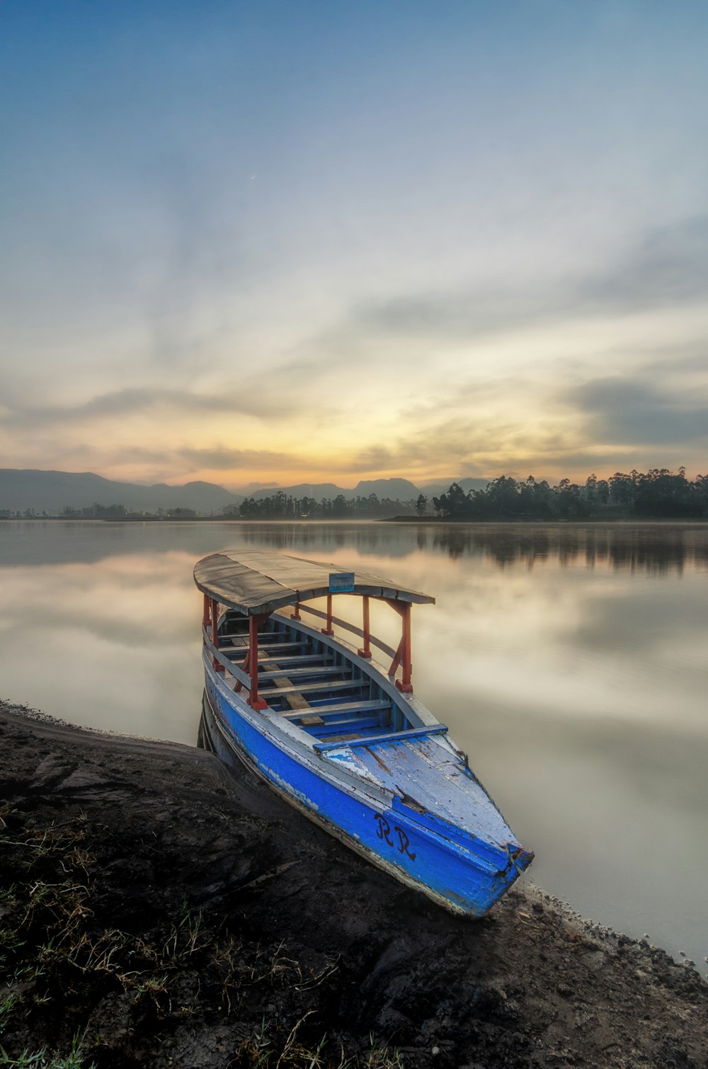 a blue boat sitting on the shore of a lake