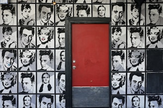 a red door is in front of a wall with black and white pictures of men