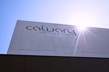 A modern building facade with the text 'Calvary Christian Church' prominently displayed. The structure features a minimalist design with clean lines and a sunburst effect in the top right corner, suggesting a sunny day.
