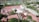 Aerial view of a sprawling complex of buildings with red roofs, surrounded by lush greenery and trees. The area includes a mosque with a distinctive green dome and minaret, situated in a small town with other residential and commercial buildings scattered around.