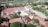 Aerial view of a sprawling complex of buildings with red roofs, surrounded by lush greenery and trees. The area includes a mosque with a distinctive green dome and minaret, situated in a small town with other residential and commercial buildings scattered around.