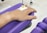 A hand rests on a purple cushion, connected to an intravenous line with a yellow cap. The background includes a tiled floor and a metallic stand, possibly part of medical equipment.