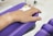 A hand rests on a purple cushion, connected to an intravenous line with a yellow cap. The background includes a tiled floor and a metallic stand, possibly part of medical equipment.