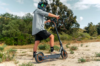 A friendly person holding an electric scooter helmet, standing beside a bright blue e-bike in a sunny Chennai street.