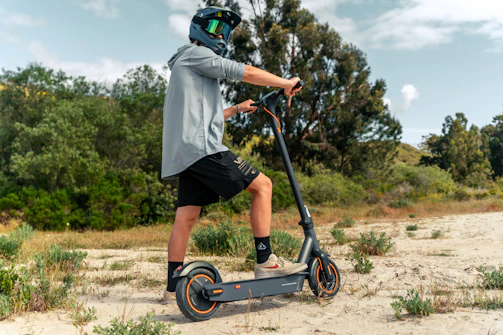 A friendly person holding an electric scooter helmet, standing beside a bright blue e-bike in a sunny Chennai street.