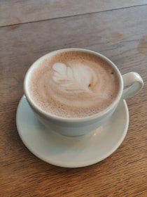 Close-up of a steaming cup of cappuccino with latte art on a wooden table.