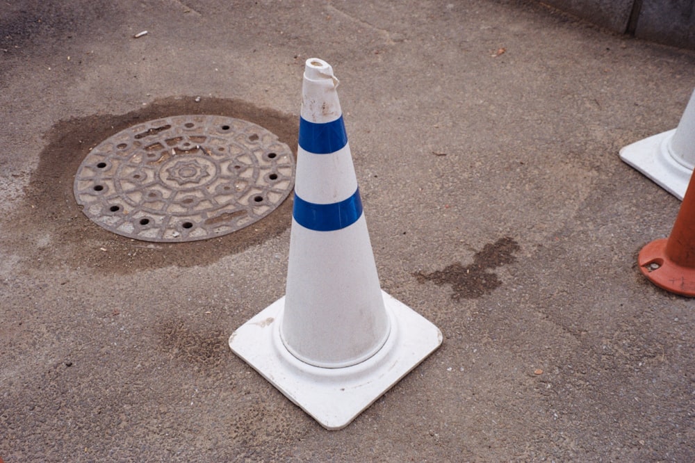a white and blue cone sitting next to a manhole