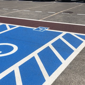 A parking area is painted with blue and white lines, featuring a sign indicating a reserved space. Cars are parked in adjacent spaces marked by yellow and white lines.
