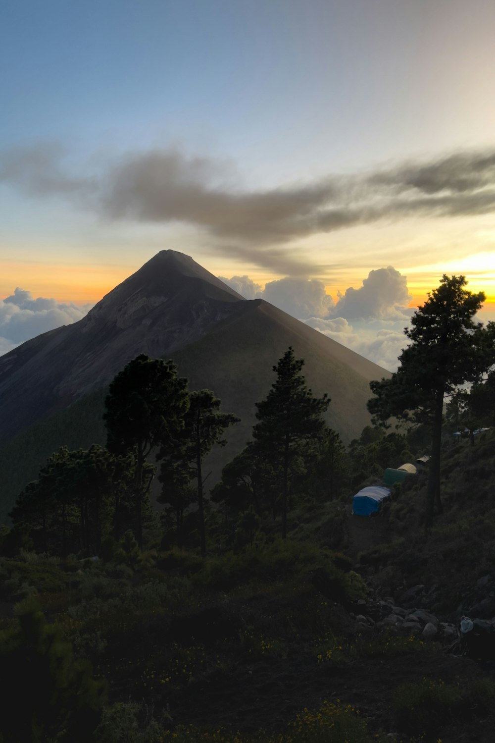 the sun is setting over a mountain with a tent in the foreground