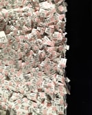 A large pile of printed paper tags, predominantly featuring printed text in black and red. Each tag includes a number and the word 'THE MET', suggesting a connection to a museum or exhibition entry system. The tags are scattered and overlapping each other, creating a sense of chaos and disorganization.
