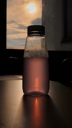 A close-up of a customized Shuddhi Ltd glass water bottle catching sunlight on a hotel dining table.
