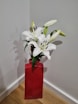 a red vase filled with white flowers on top of a wooden floor