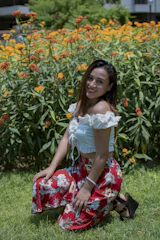 A smiling landscaper kneeling beside a freshly planted flower bed in a sunny yard.