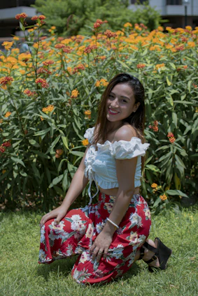 A smiling landscaper kneeling beside a freshly planted flower bed in a sunny yard.
