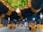 A luxurious indoor banquet hall features a stunning ceiling decorated with lush greenery and sparkling lights. Elegant chandeliers hang from the ceiling, providing a warm glow. The seating area is arranged with vibrant orange chairs around circular tables, all set on an intricately patterned carpet. The walls are adorned with a combination of dark drapery and golden geometric patterns.