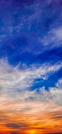 A vibrant sky transitions from warm orange and yellow tones at the horizon to deep blues and purples toward the top, with wispy clouds enhancing the gradation.