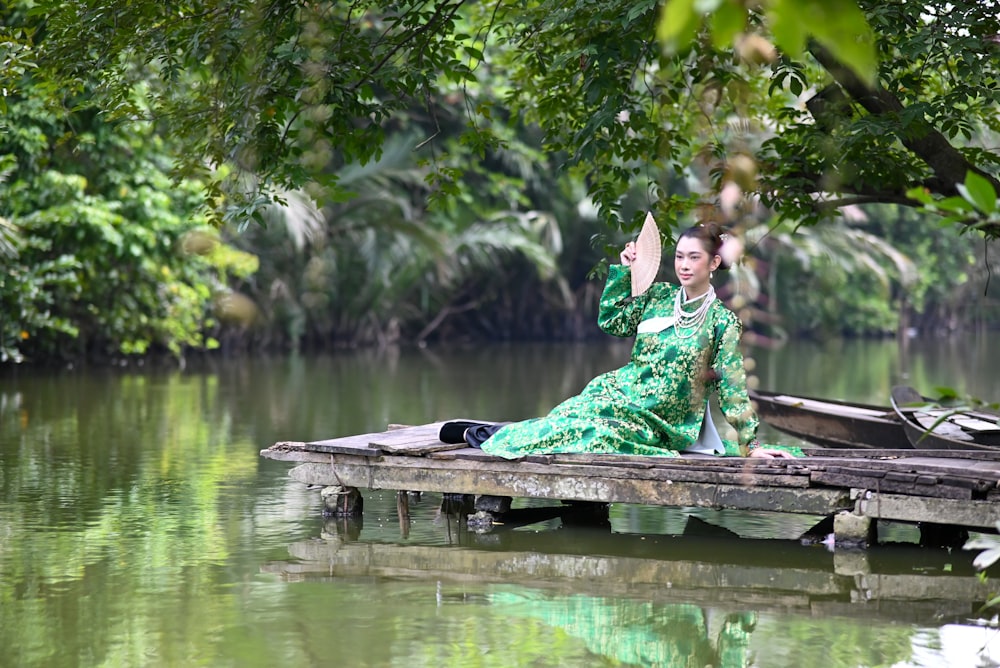a woman in a green dress sitting on a dock