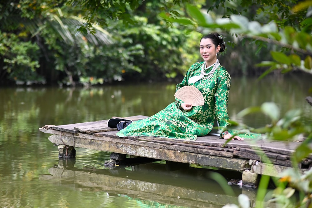 a woman in a green dress sitting on a dock