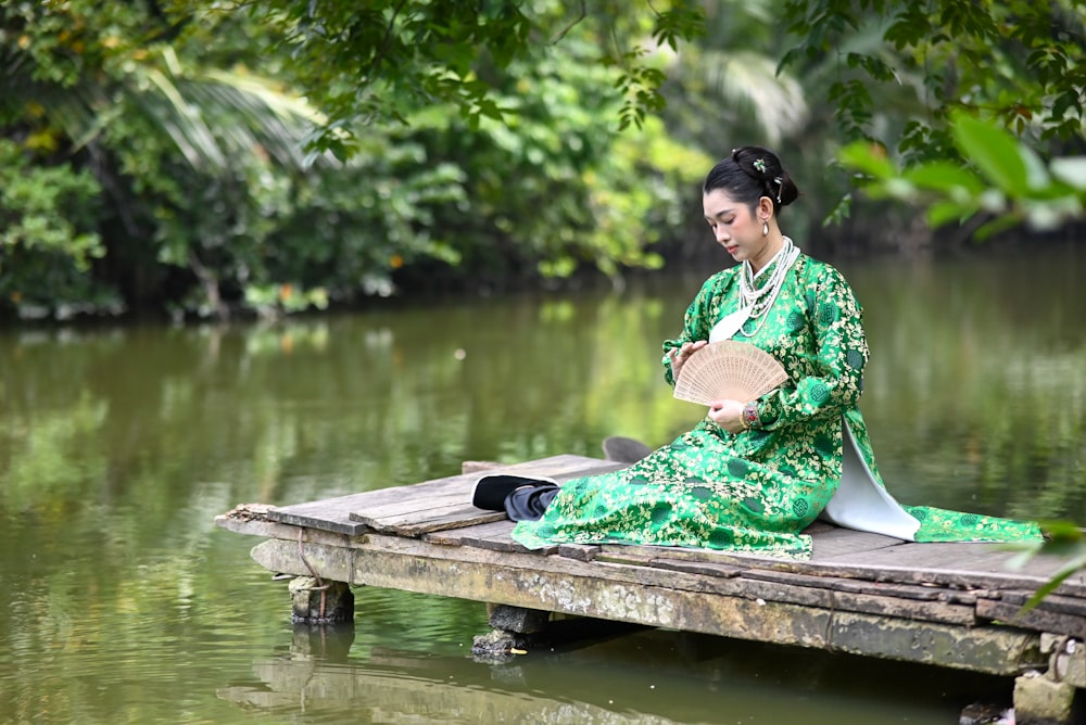 a woman in a green dress is sitting on a dock