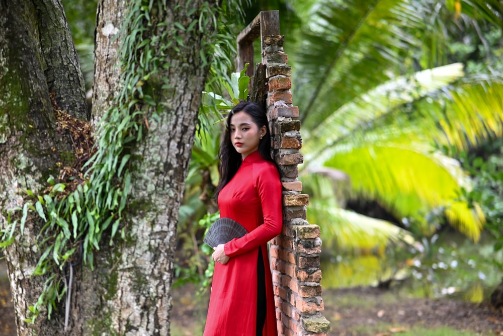 una mujer con un vestido rojo apoyada en un árbol