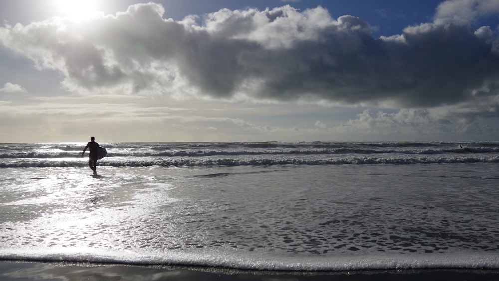 a person walking into the ocean with a surfboard