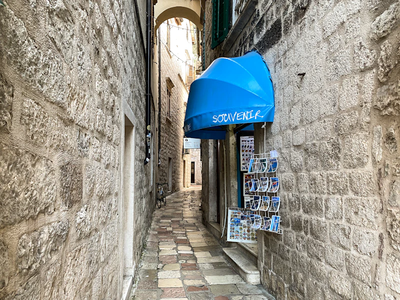 A narrow cobbled alley in Kotor's Old Town with a blue souvenir-shop awning