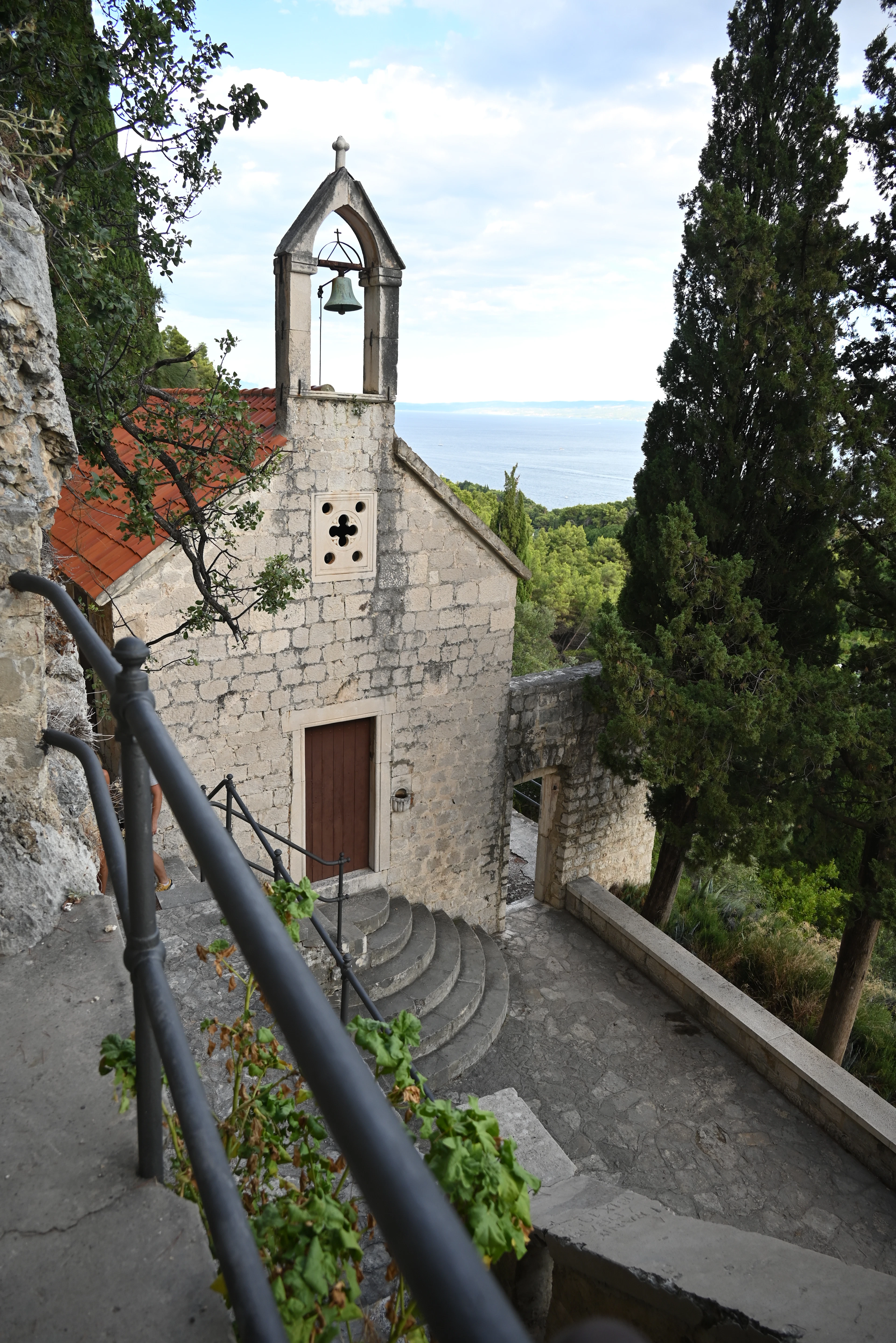 The small stone church of St Jerome on the Marjan hillside above Split, its open bell-cote and rounded stone steps set among cypresses, with the Adriatic spread out beyond.