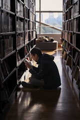 a man sitting on the floor in a library reading a book