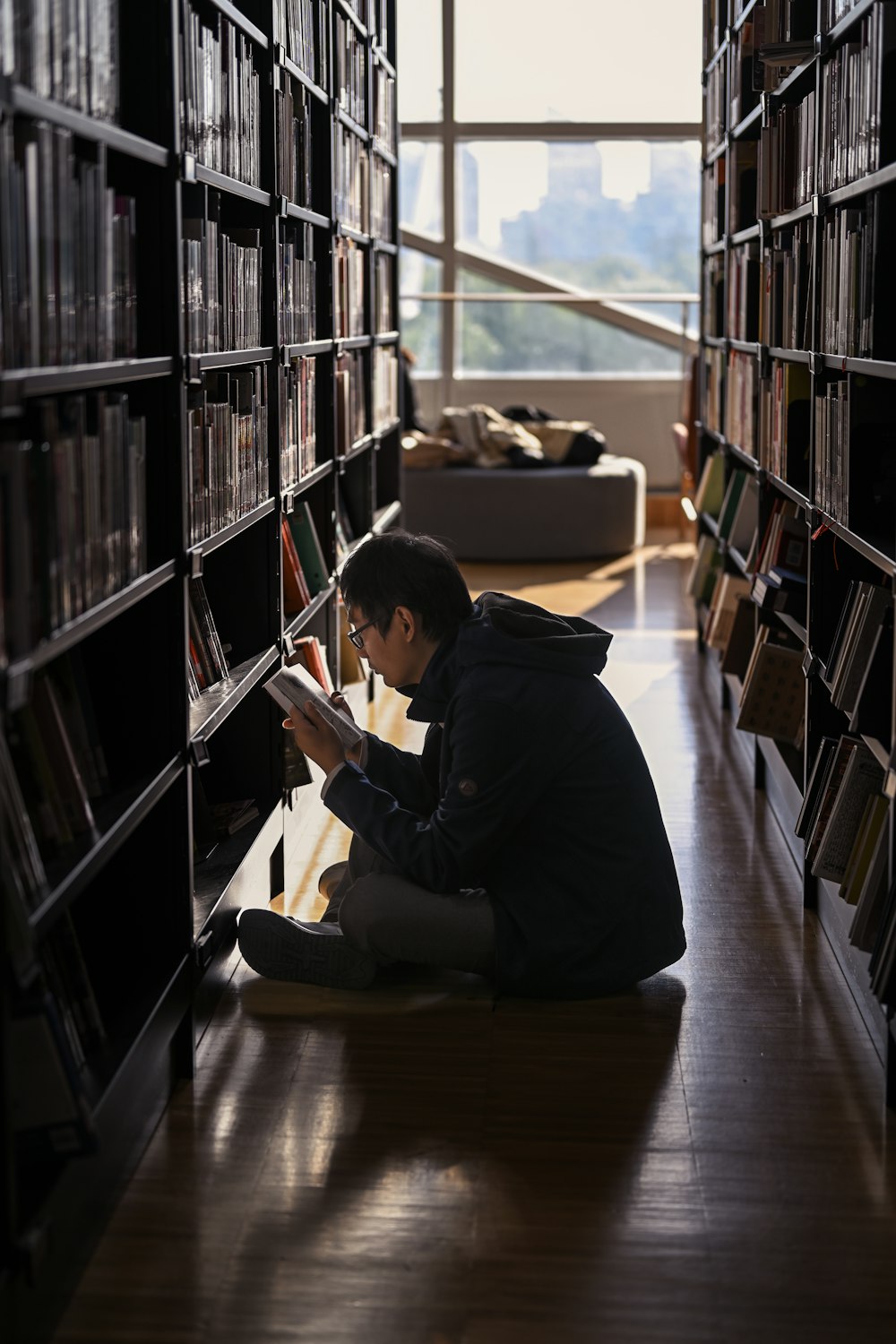 un hombre sentado en el suelo en una biblioteca leyendo un libro