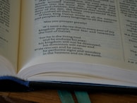 A close-up view of an open book, focusing on a specific passage with bold text. The book appears to be well-used, with a blue fabric cover partially visible underneath. The text includes a decree by a king and mentions God, kingdom, and signs and wonders.