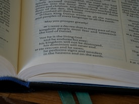 A close-up view of an open book, focusing on a specific passage with bold text. The book appears to be well-used, with a blue fabric cover partially visible underneath. The text includes a decree by a king and mentions God, kingdom, and signs and wonders.