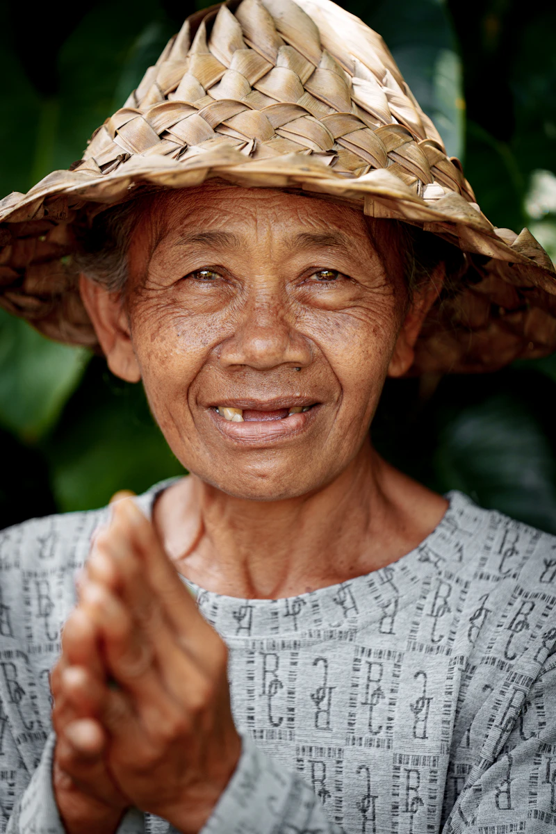 A cheerful older woman in a straw hat smiling outdoors on a sunny day