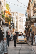 A friendly taxi driver assisting a passenger with luggage amid Greek island scenery.