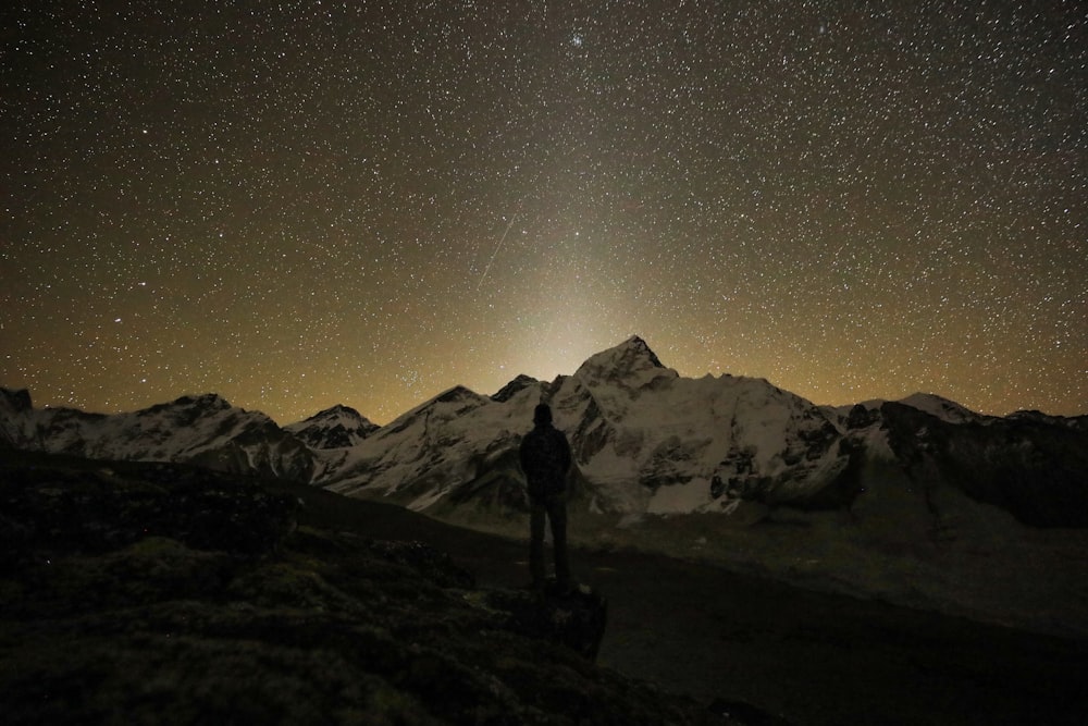 a man standing on top of a mountain under a night sky