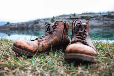 Pair of worn brown cowboy boots leaning against a wooden fence in a country setting