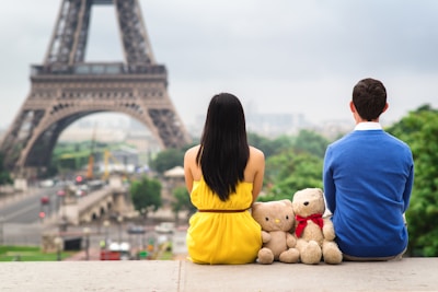 a man and a woman sitting on a ledge in front of the eiffel