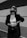 A person is standing confidently against a minimalist architectural background. They are wearing sunglasses, a dark blazer, a white crop top, and high-waisted pants. Their pose exudes confidence and style, with one hand resting on their hip and the other holding a stylish bag.