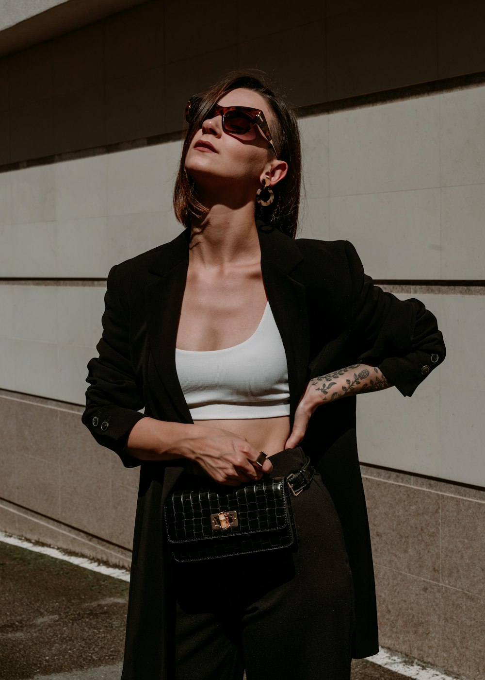 uma mulher de top branco e blazer preto segurando uma bolsa preta