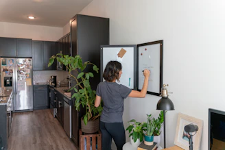 A person writing meal prep notes on a clipboard beside fresh vegetables and kitchen tools.