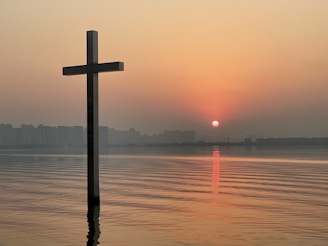 A peaceful sunrise over calm water with a softly glowing cross silhouette.