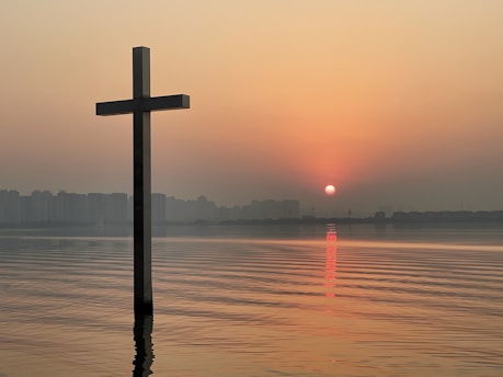 A peaceful sunrise over calm water with a softly glowing cross silhouette.
