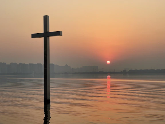 A softly lit graphic featuring a gentle sunrise over calm waters with a subtle cross silhouette.