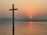 A serene sunrise over a calm sea with a gentle cross silhouette in the foreground.