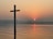A serene sunrise over a calm sea with a gentle cross silhouette in the foreground.