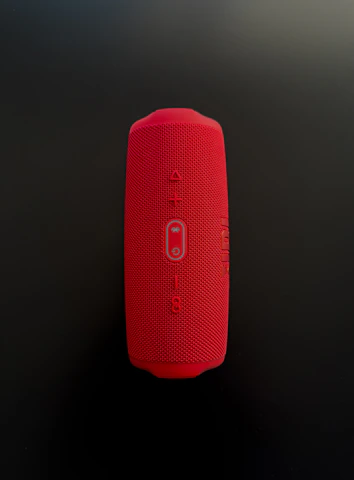 Close-up of a hand adjusting the volume on a compact, modern Bluetooth speaker.
