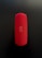 A red cylindrical Bluetooth speaker with a mesh texture, featuring control buttons for power, volume, and wireless connectivity in the center. The speaker is placed vertically against a dark background.